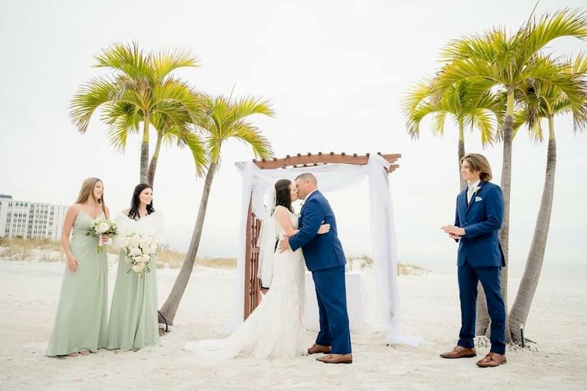 A beach wedding ceremony with a couple at the altar, a bridesmaid, and an officiant.