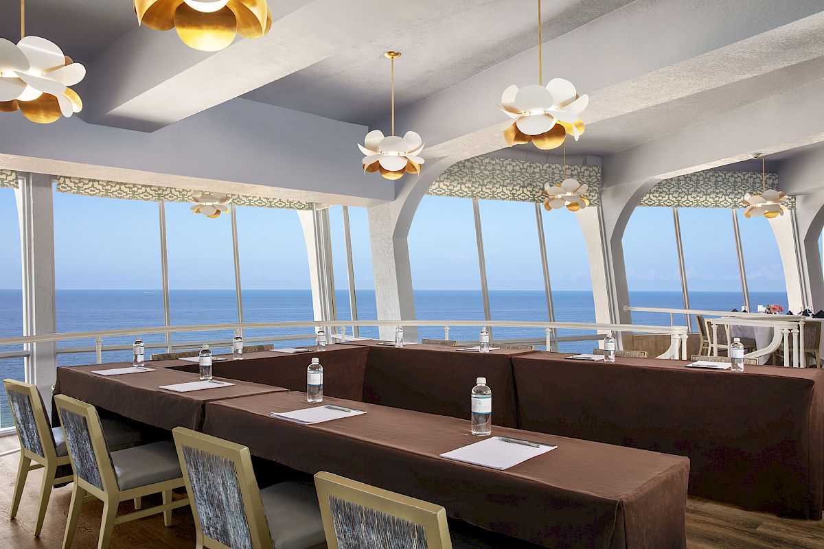 Elegant dining room with sea view, stylish chairs, and unique light fixtures.