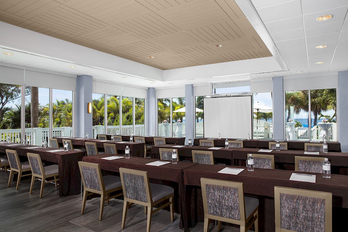 An empty conference room with tables, chairs, and a projection screen.