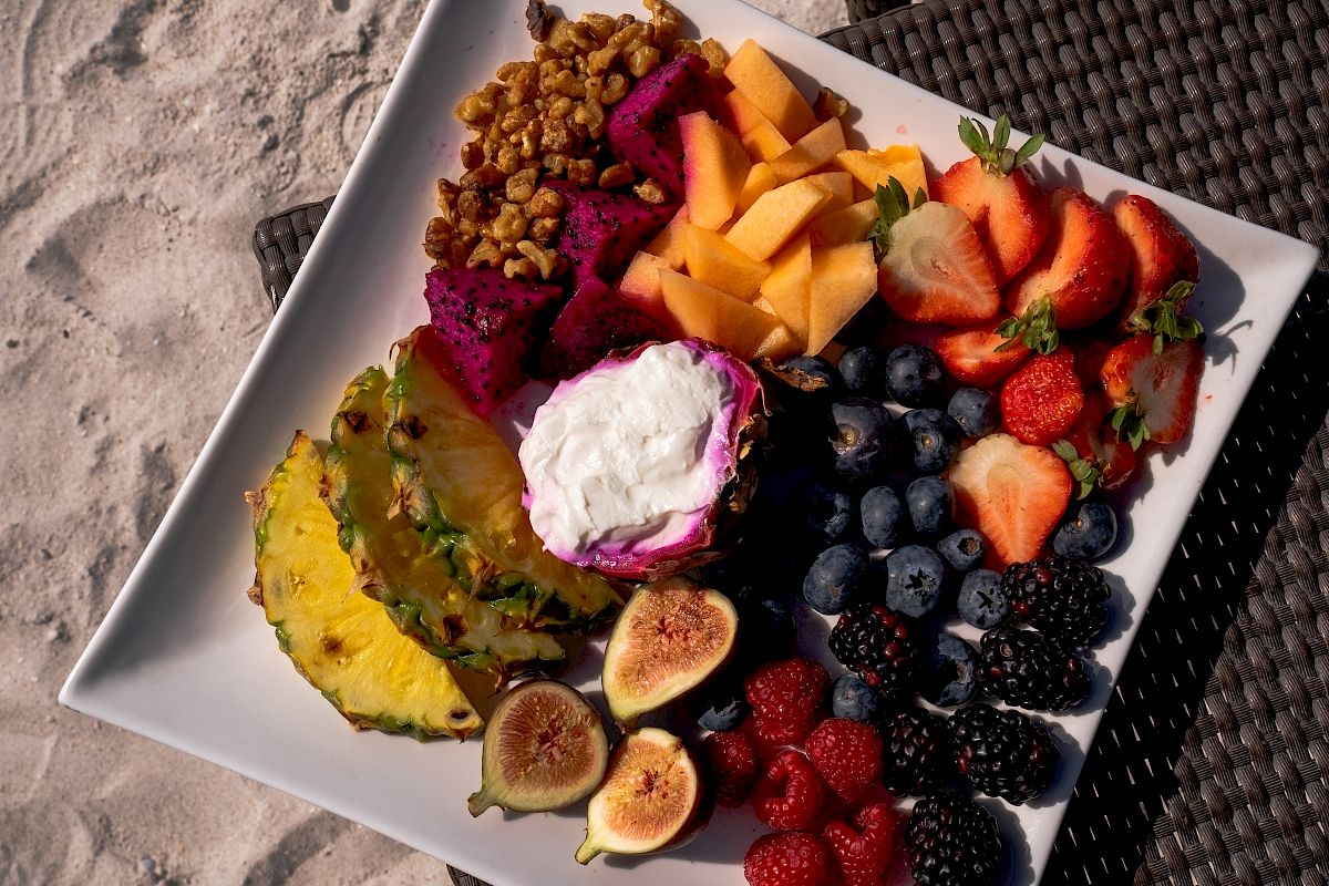 A plate with assorted fruits like strawberries, figs, and pineapple, served on a table.