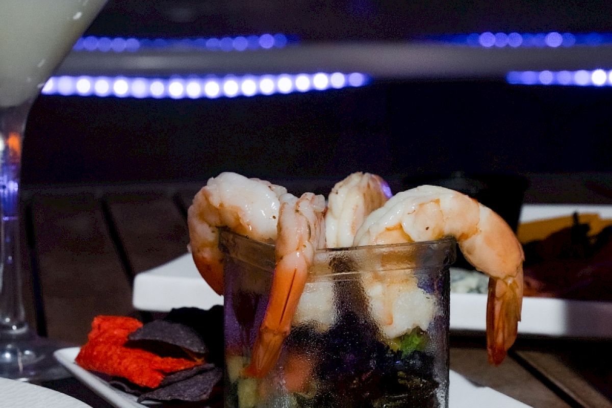 Shrimp cocktail over a glass, assorted fruits, and a sunset view in the background.