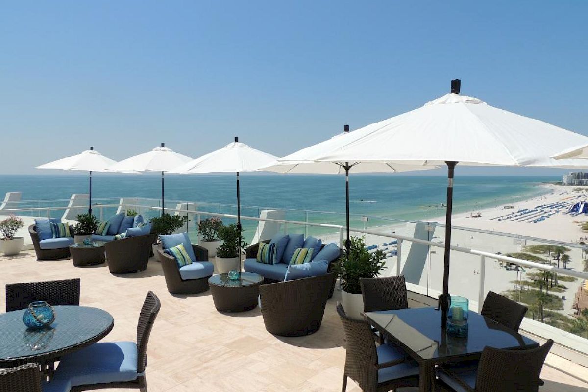 Ocean view terrace with tables, chairs, and white umbrellas.
