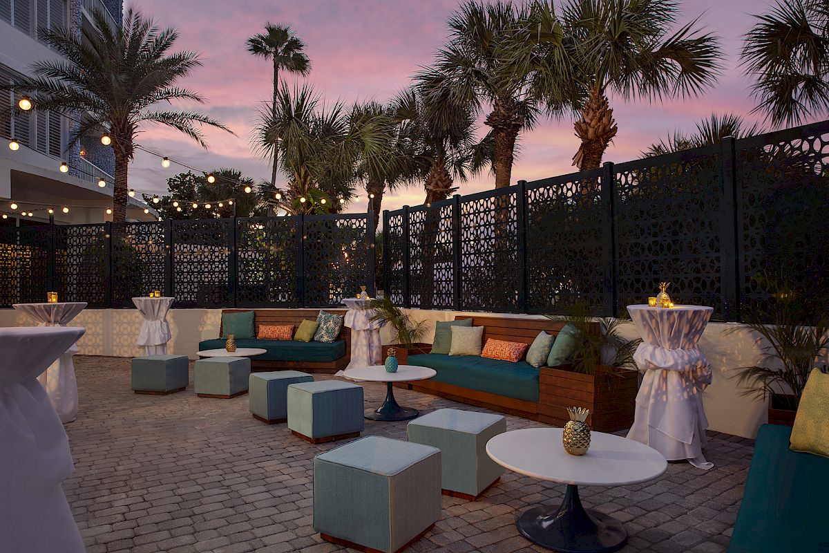 An outdoor lounge area with upholstered seating, tables, and decorative screens, set under a twilight sky.