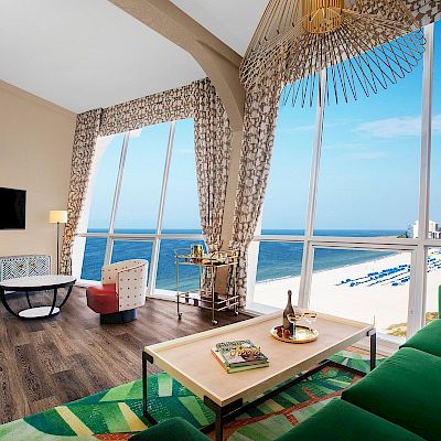 Bright beachfront room with a sofa, table, TV, ocean view, and colorful interior design.
