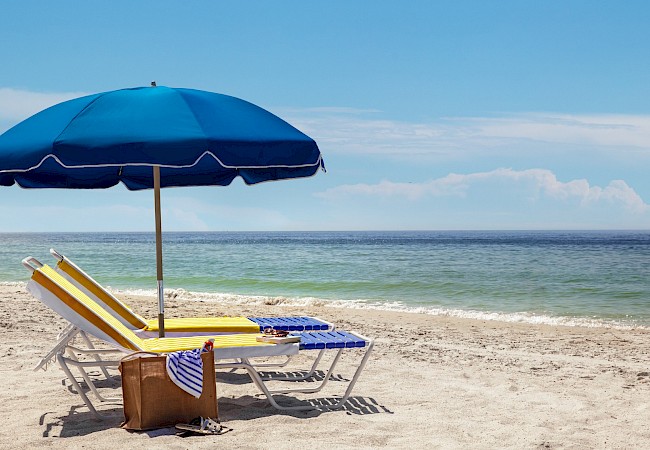 A beach scene with a blue umbrella, chair, and the ocean in the background.