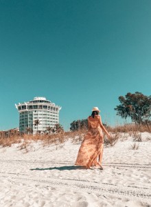 A person is walking on the beach with a building in the background.