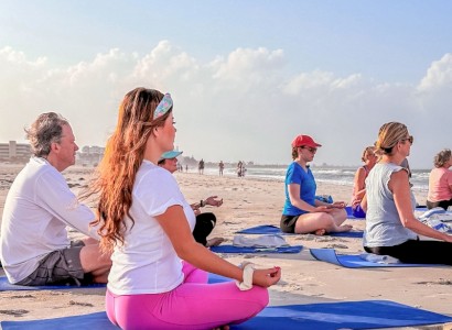 People are practicing yoga on a sandy beach under a clear sky.