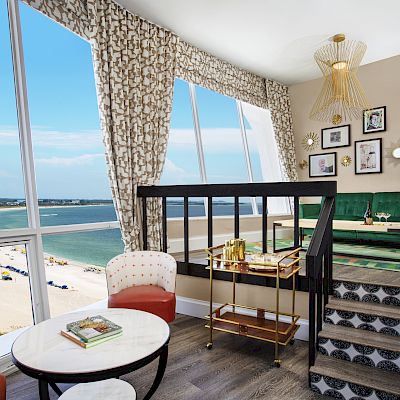 Cozy room with chic decor, a window view of the beach, stylish furniture, and wall art.