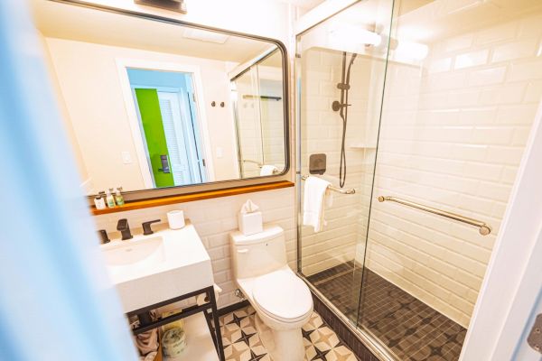A well-lit bathroom with a sink, mirror, toilet, glass shower, and patterned floor tiles.