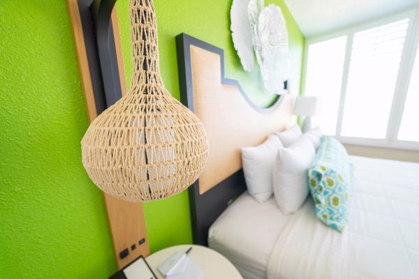 Bright bedroom with a green wall, wicker lamp, white pillows, and abstract art.
