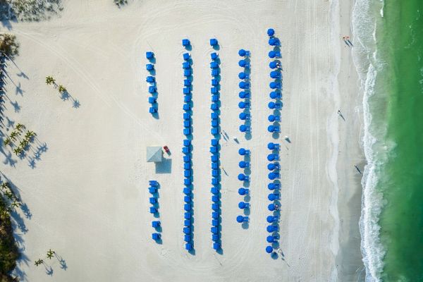 Aerial view of a beach with blue umbrellas and a hut, near the shore.