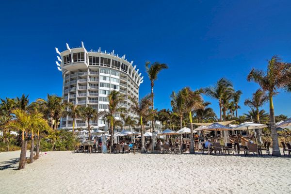 Tropical beach setting with a unique building, palm trees, and outdoor seating areas.