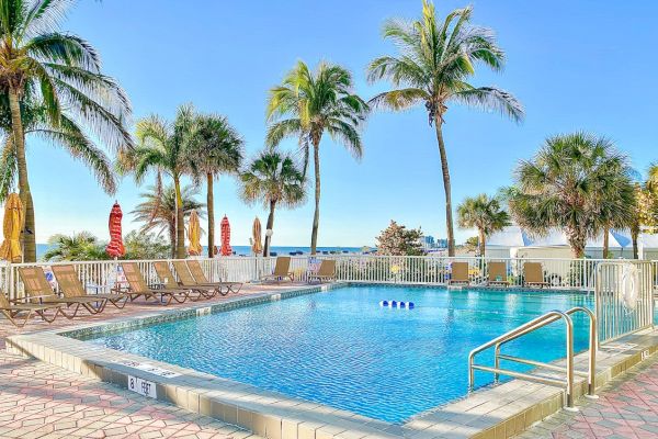 Sunny poolside with palm trees, lounge chairs, and clear blue sky.