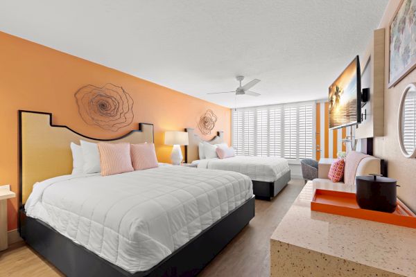 A bright, modern bedroom with two beds, accent pillows, and floral art on the walls.