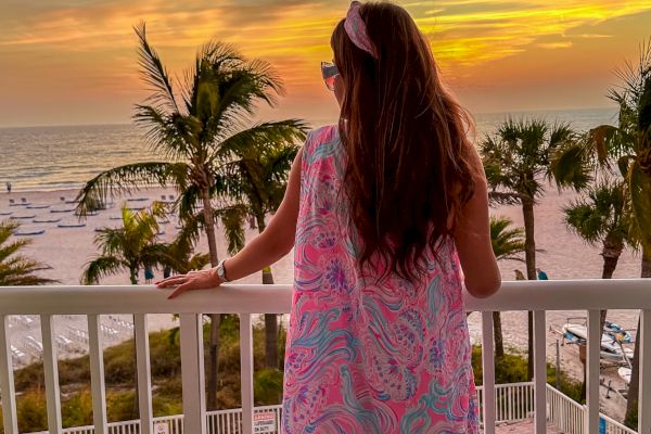 A person admires a sunset from a balcony overlooking a beach.