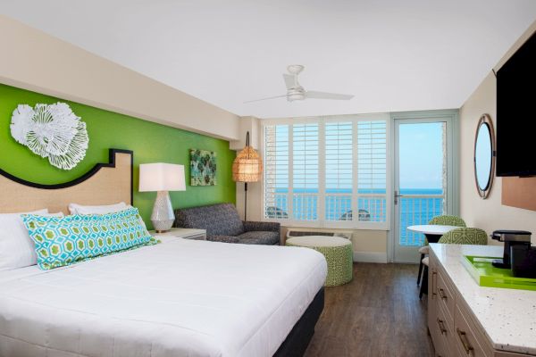 A bright hotel room with a bed, ceiling fan, furniture, and ocean view.