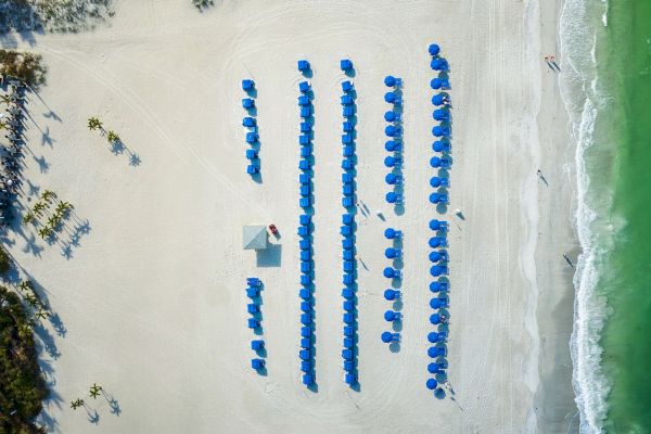 Aerial view of a beach with rows of blue umbrellas and a lifeguard hut.