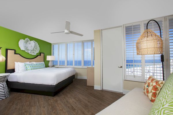 Bright beachside room with a bed, green accent wall, ceiling fan, and ocean view.
