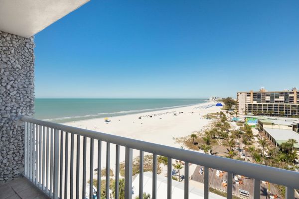 View from a balcony showing a sandy beach, the ocean, and buildings under a clear sky.