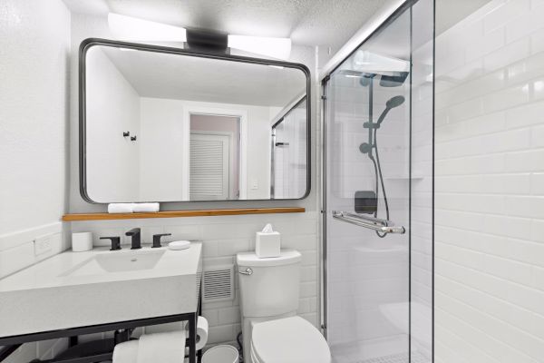 Modern bathroom with a shower, sink, mirror, and toilet in white tones.