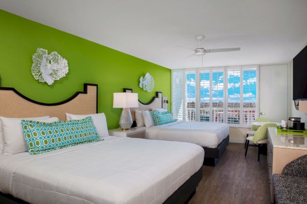 A bright hotel room with two beds, colorful decor, and a sunny window view.