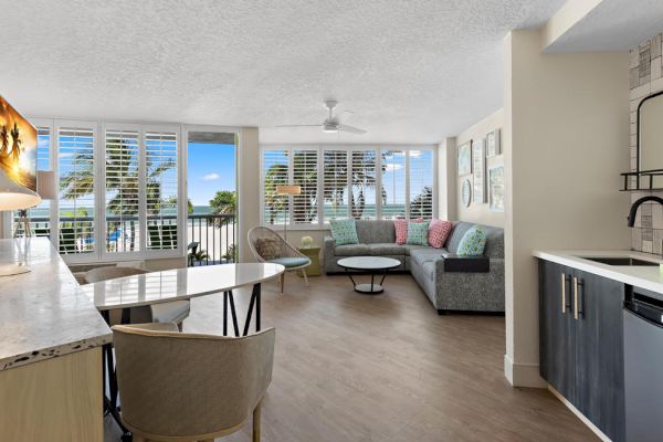 Modern living room with kitchen, couch, and balcony overlooking palm trees.