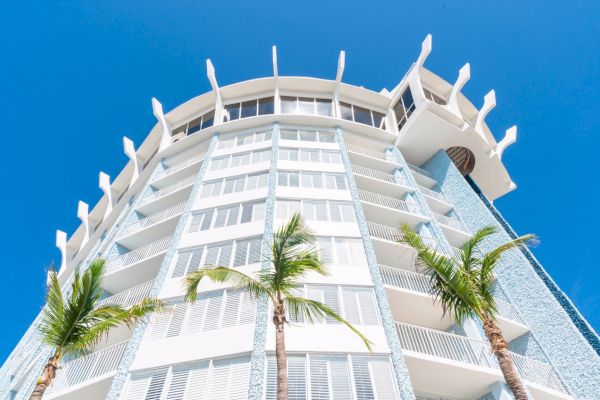 Modern high-rise building with balconies against a blue sky, flanked by palm trees.