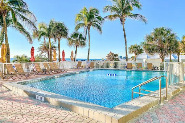 A pool with lounge chairs, palm trees, and blue sky in the background.