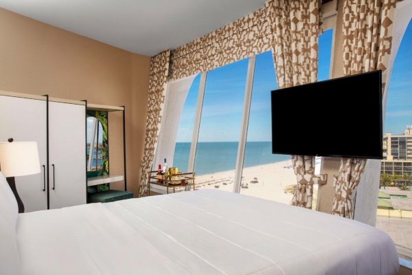 Hotel room with a bed, TV, and ocean view windows.