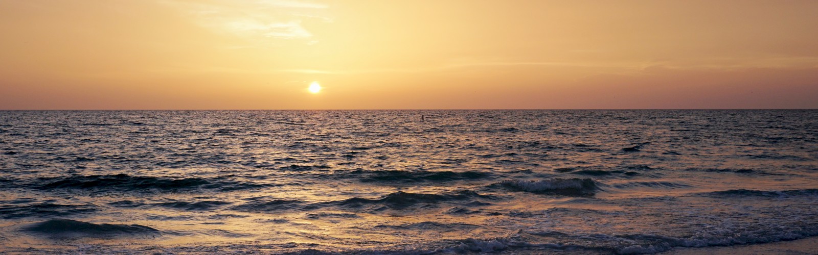 Sunset over the ocean with waves and a clear horizon.