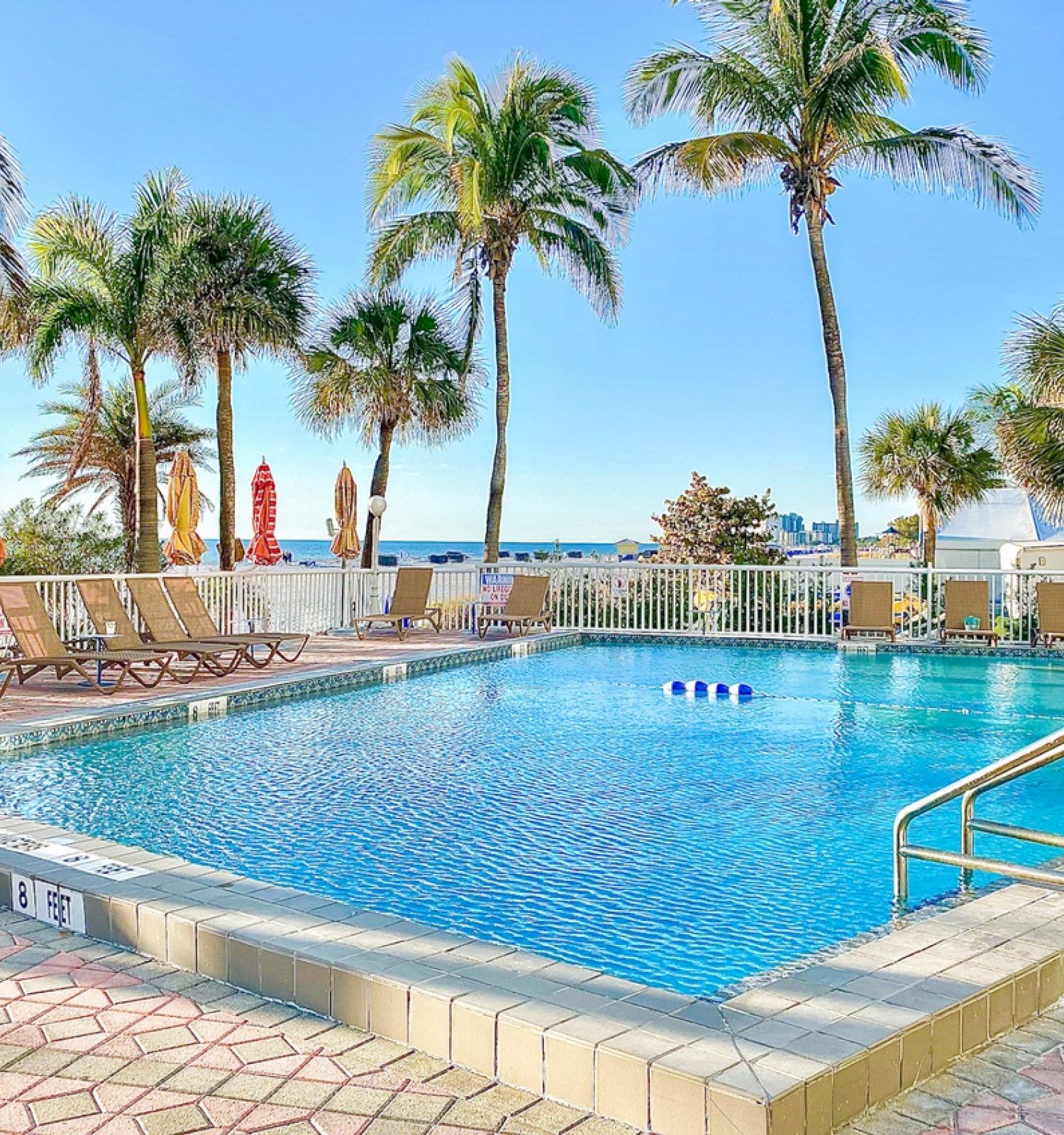 A tranquil poolside scene with palm trees, loungers, and the ocean in the background.