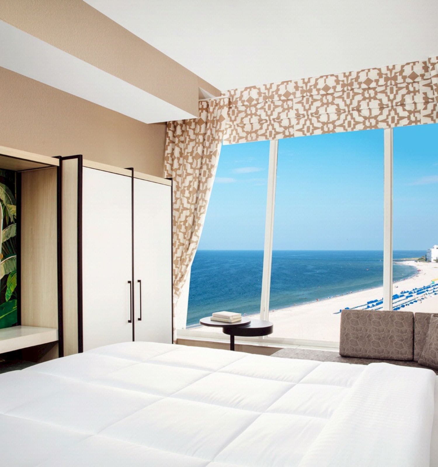 A modern hotel room with a large window overlooking the beach and ocean.