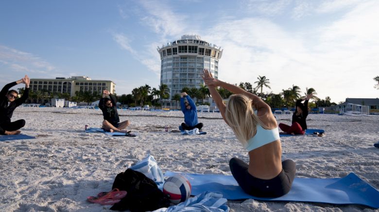 People doing yoga on the beach with a building in the background.