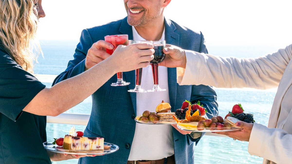 Three people are toasting with drinks, with a sea view and food.