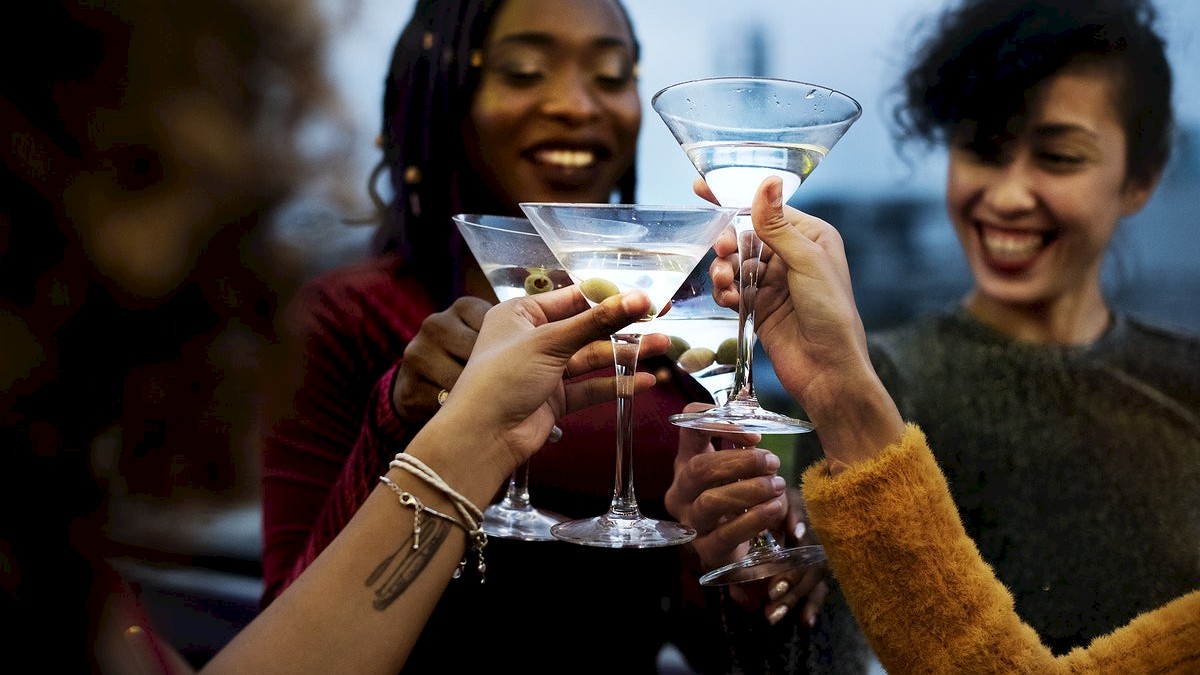 People are toasting with martini glasses, smiling, in a celebratory gathering.