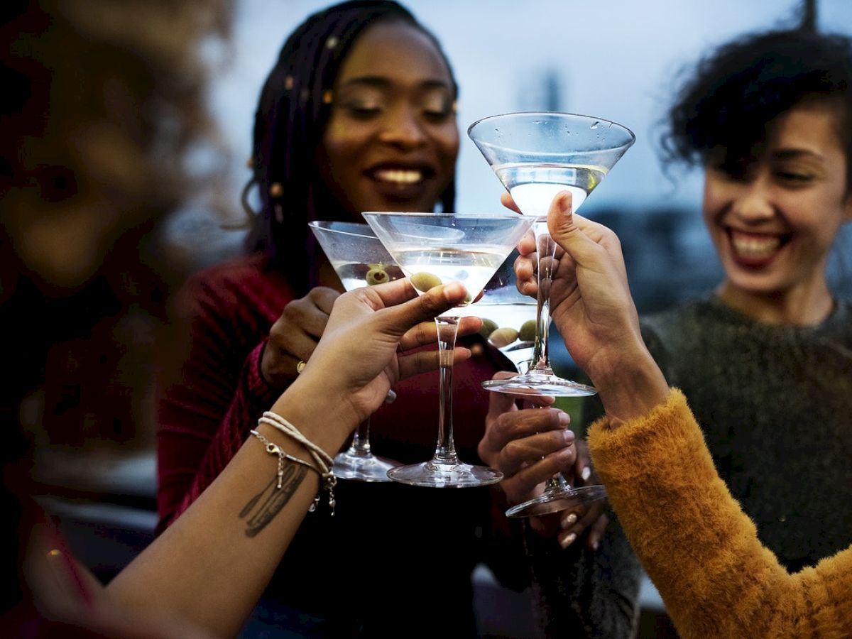 People are toasting with martini glasses, smiling, in a celebratory gathering.