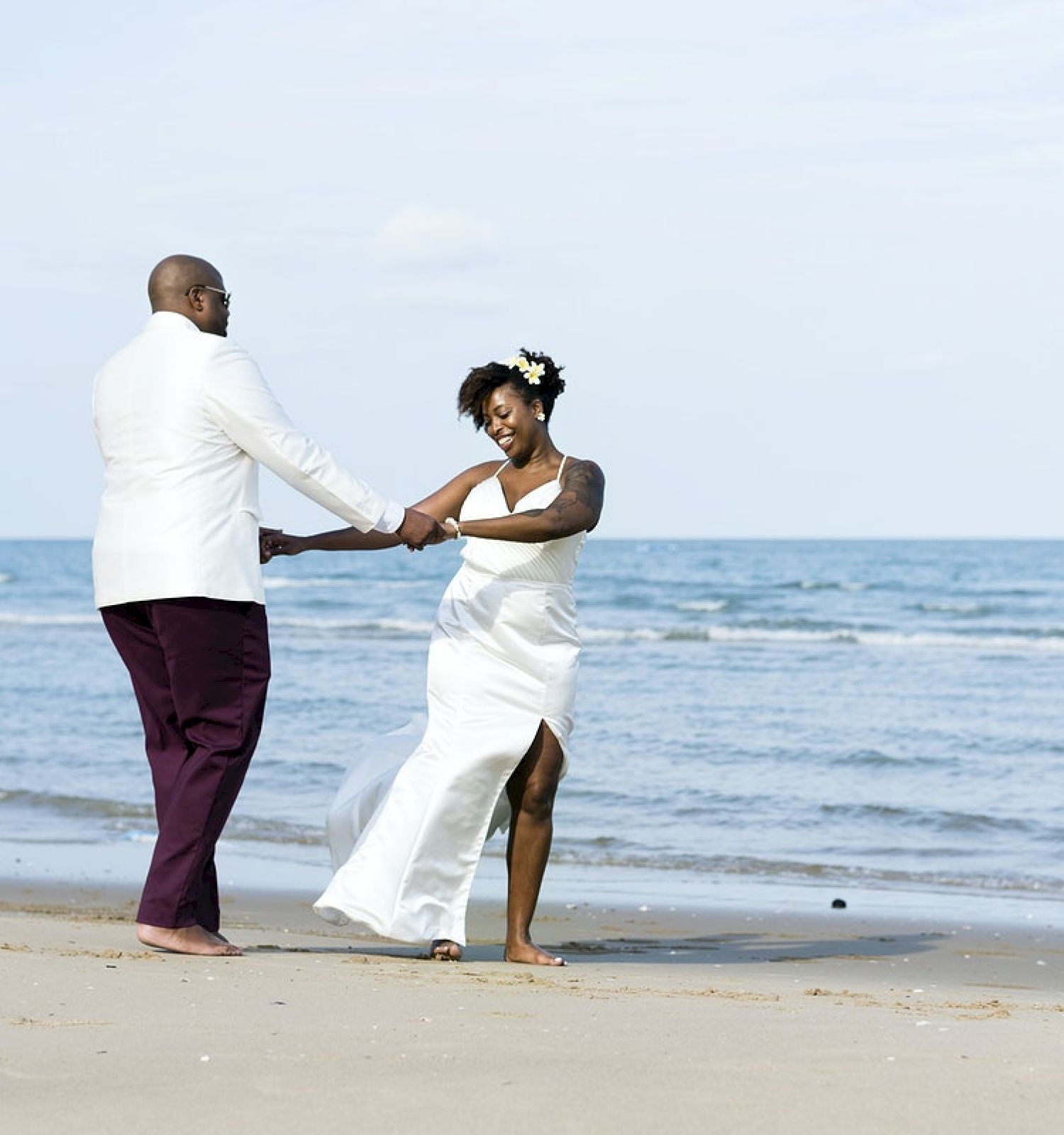 A couple is holding hands on the beach, likely celebrating a special occasion.