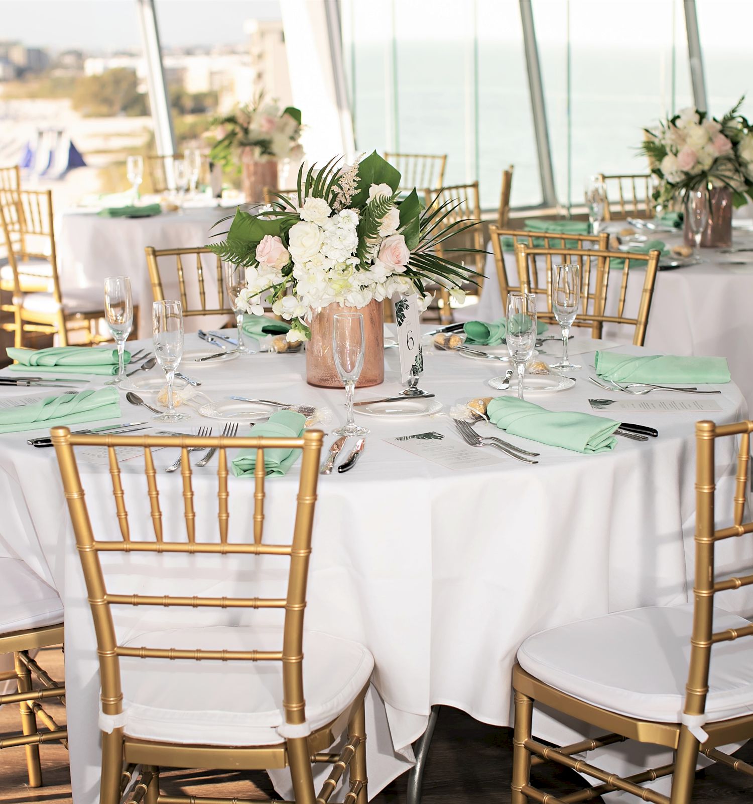 Elegant table setting with golden chairs, floral centerpieces, and ocean view.