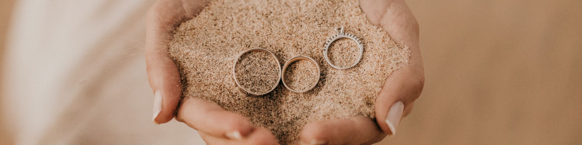 Hands holding sand with three rings.