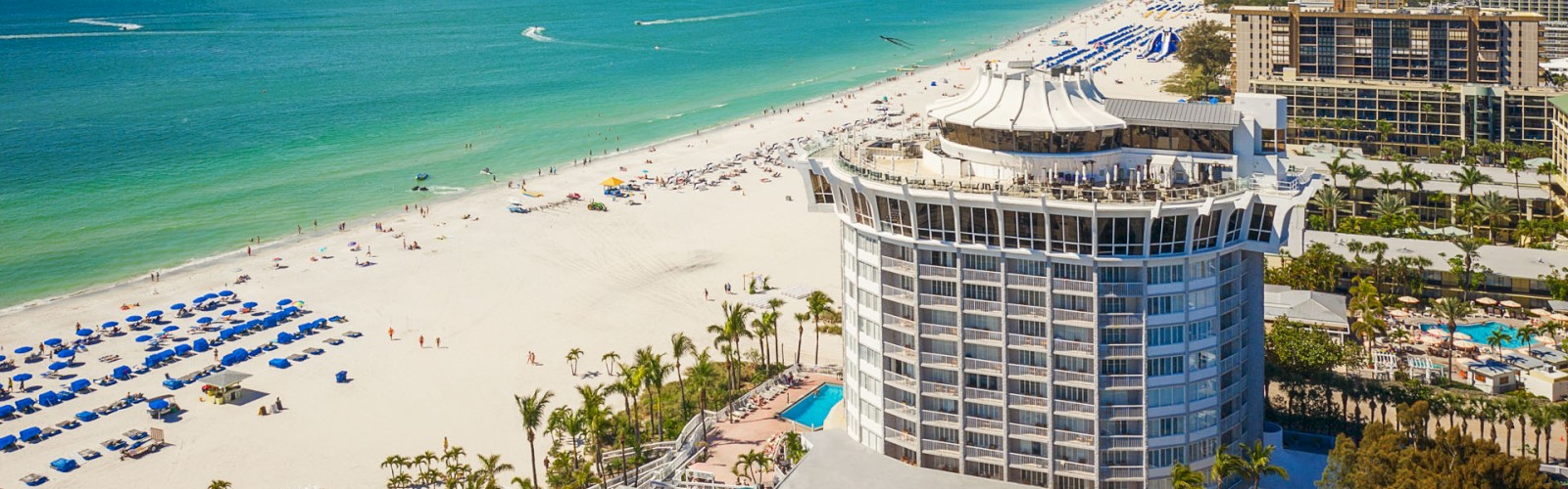 Sunny beachfront with umbrellas, a high-rise building, and a clear blue sky.
