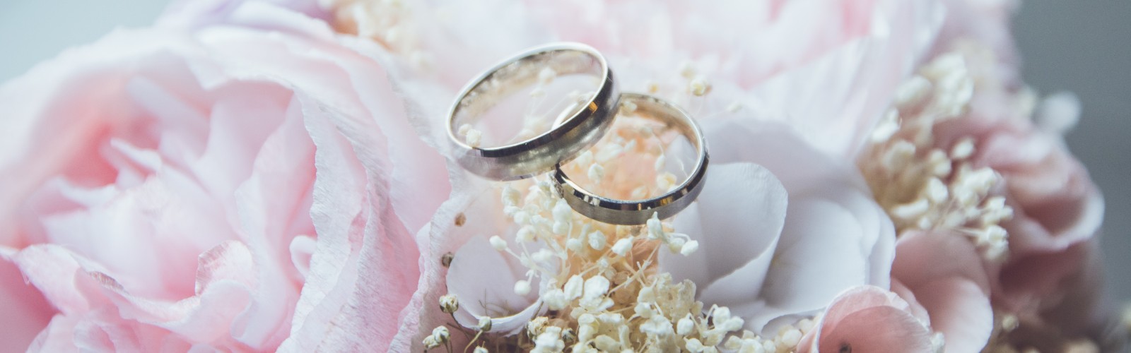 Two wedding rings rest on a bouquet of blush roses and baby's breath.