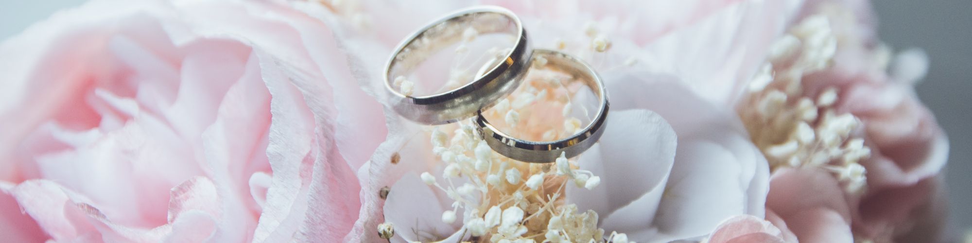 Two wedding rings rest on a bouquet of blush roses and baby's breath.