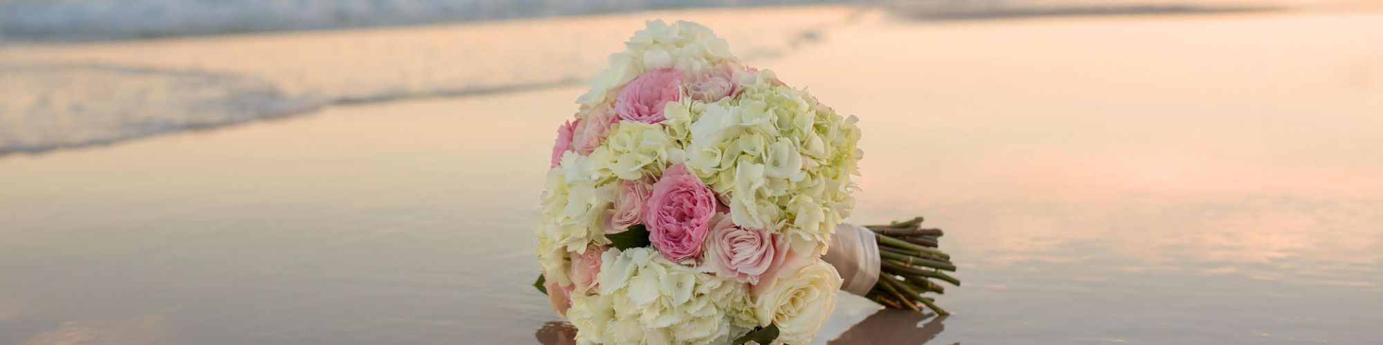 A bridal bouquet on the beach with waves in the background during sunset.