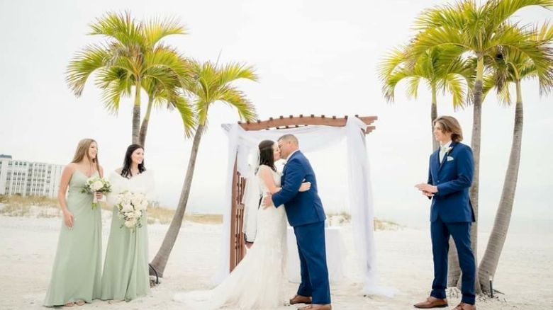 A beach wedding ceremony with a couple at the altar, a bridesmaid, and an officiant.