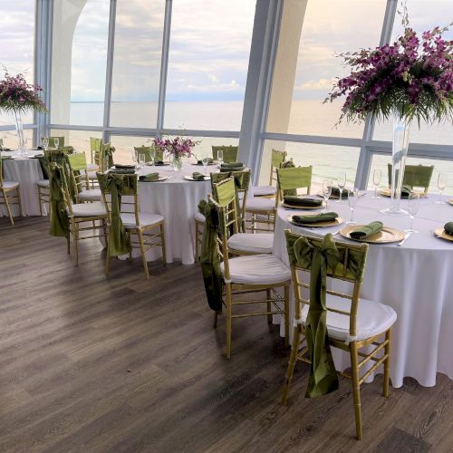 Elegantly set tables with white linens and golden chairs in a venue with ocean views.