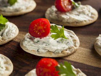 Crackers with cream cheese, tomatoes, and parsley on a wooden board.