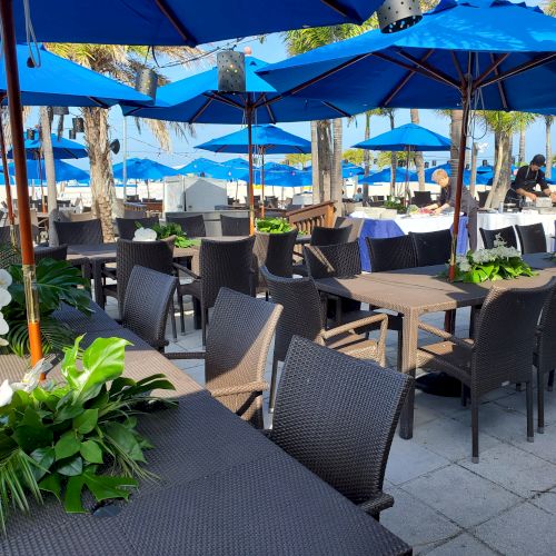 Outdoor seating with tables, chairs under blue umbrellas, and plants.