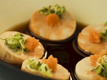 Slices of sushi with green garnish and a dollop of orange roe set in dark sauce.