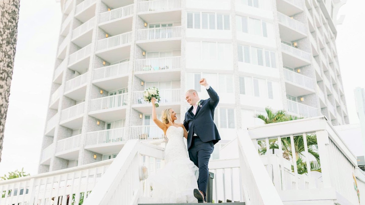 A joyful couple in wedding attire celebrating on stairs with a building backdrop.