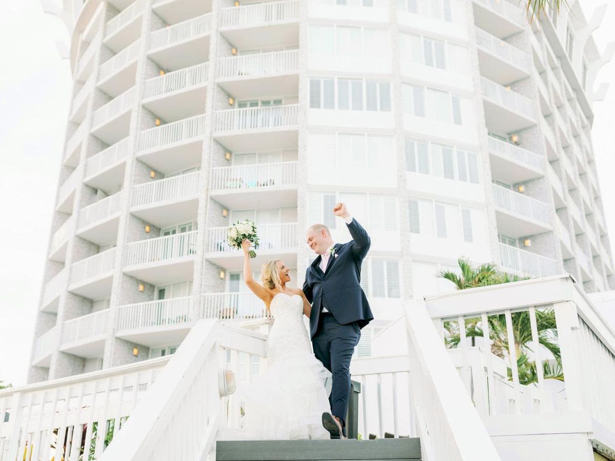 A joyful couple in wedding attire celebrating on stairs with a building backdrop.